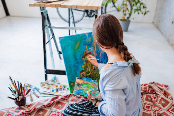 Person painting a paint-by-numbers landscape canvas for relaxation and mental wellness.